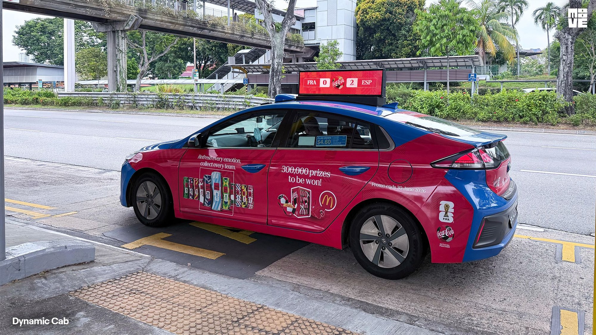 Dynamic Cab taxi in Singapore wrapped in the Coca-Cola FIFA World Cup 26 side decal, with a live match score on its digital roof screen