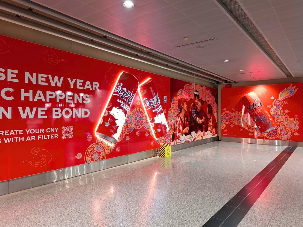 Coca-Cola Chinese New Year MRT station corridor, the wall decal continuing down the hallway into a second panel with the dragon pattern and a single illuminated Coca-Cola can